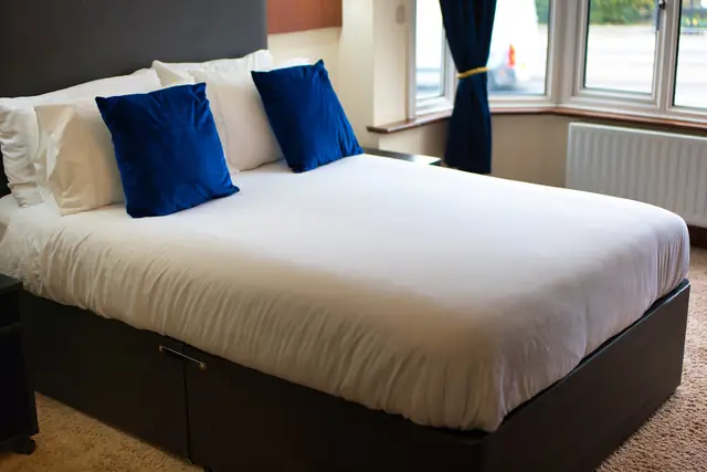 Neatly made double bed by a bright bay window with net curtains